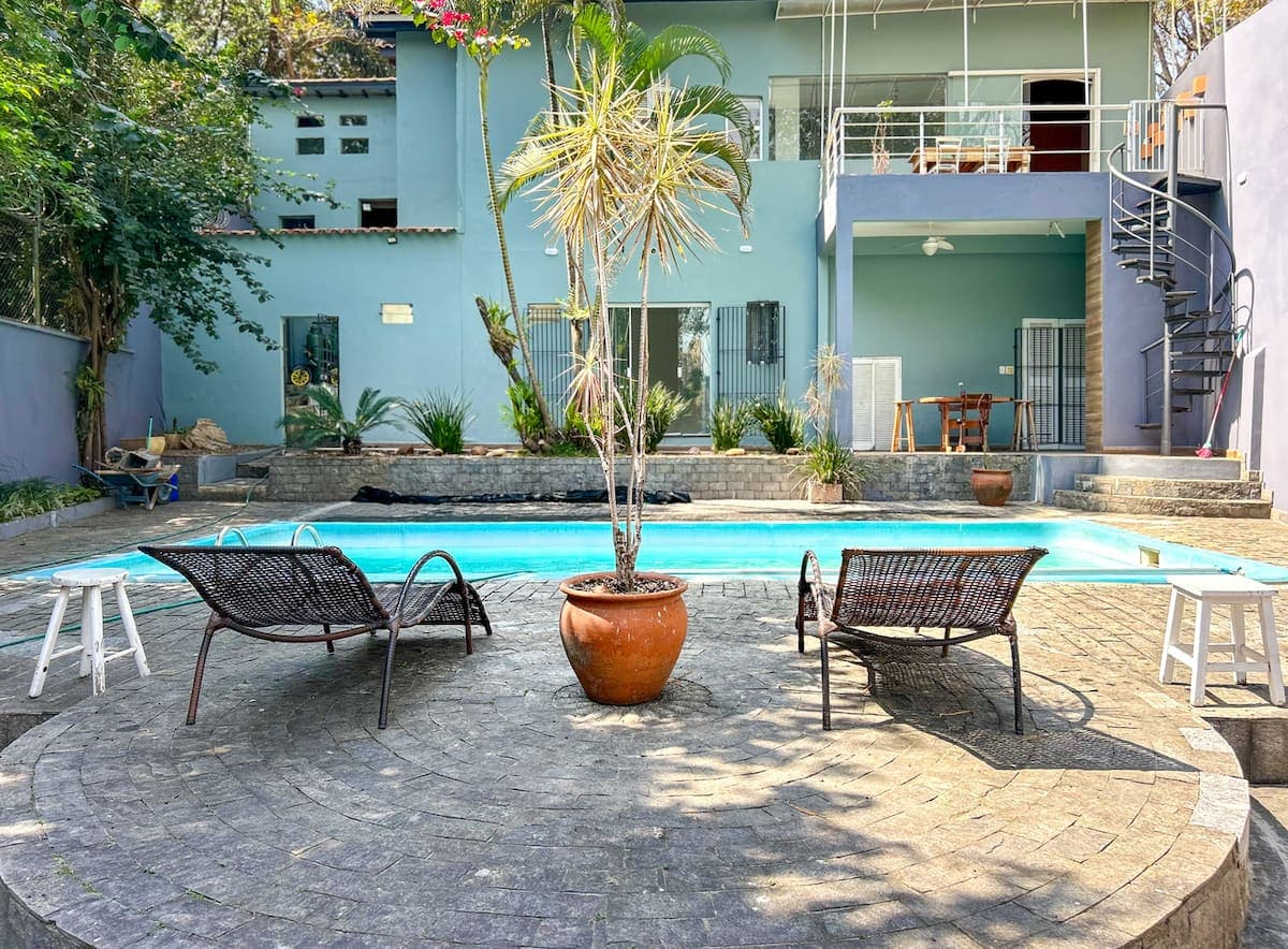 Piscina com deck de pedra, poltronas e palmeira