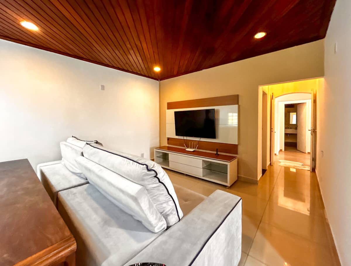 Sala de TV com sofa claro e painel de madeira