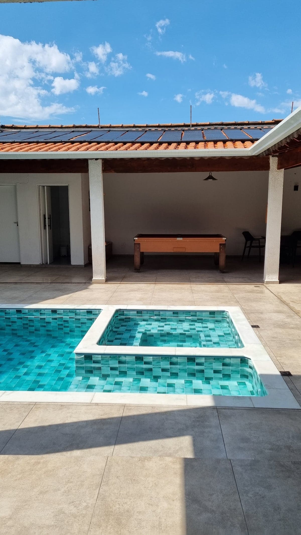 Piscina com prainha e mesa de madeira na area coberta
