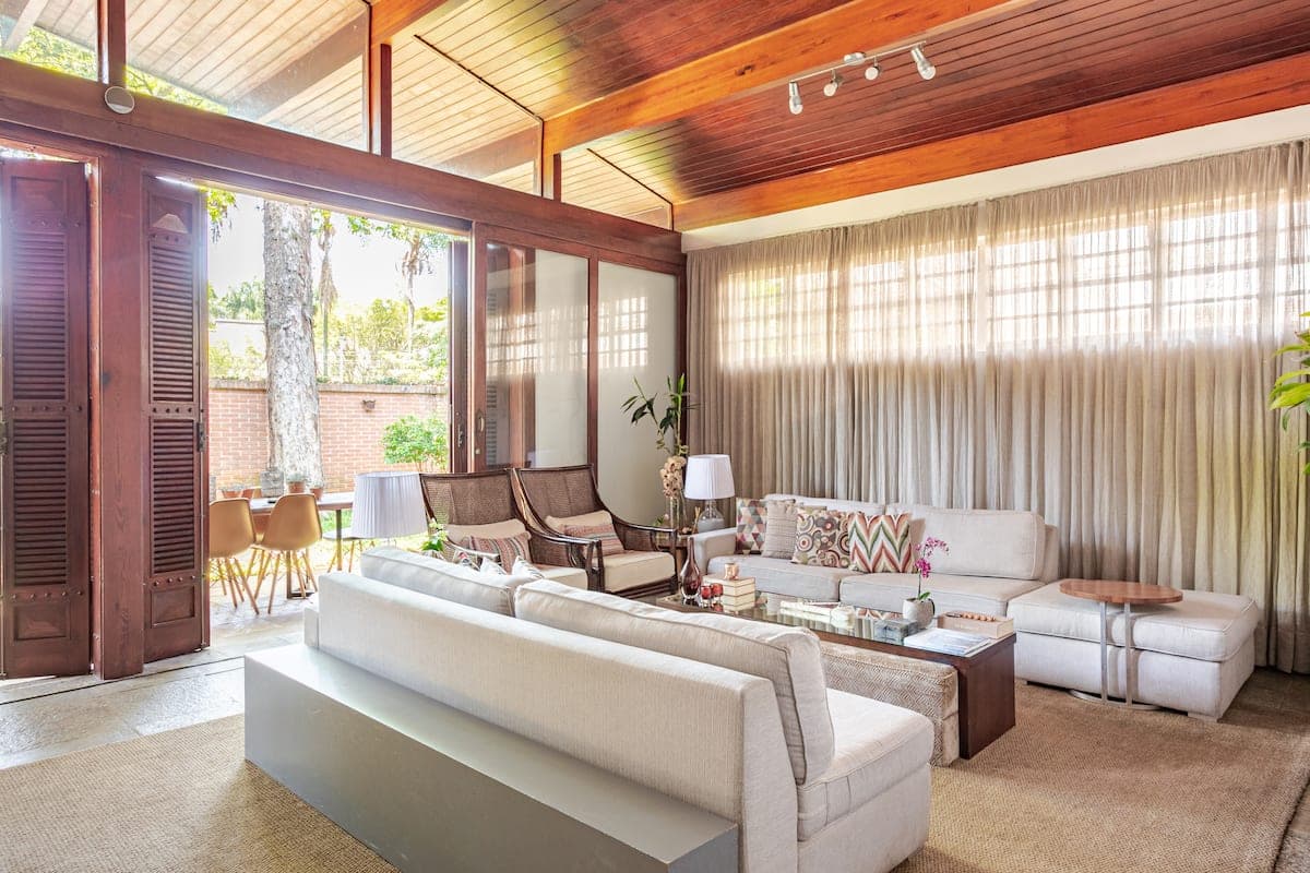 Sala de estar com sofas claros e janelas para o quintal