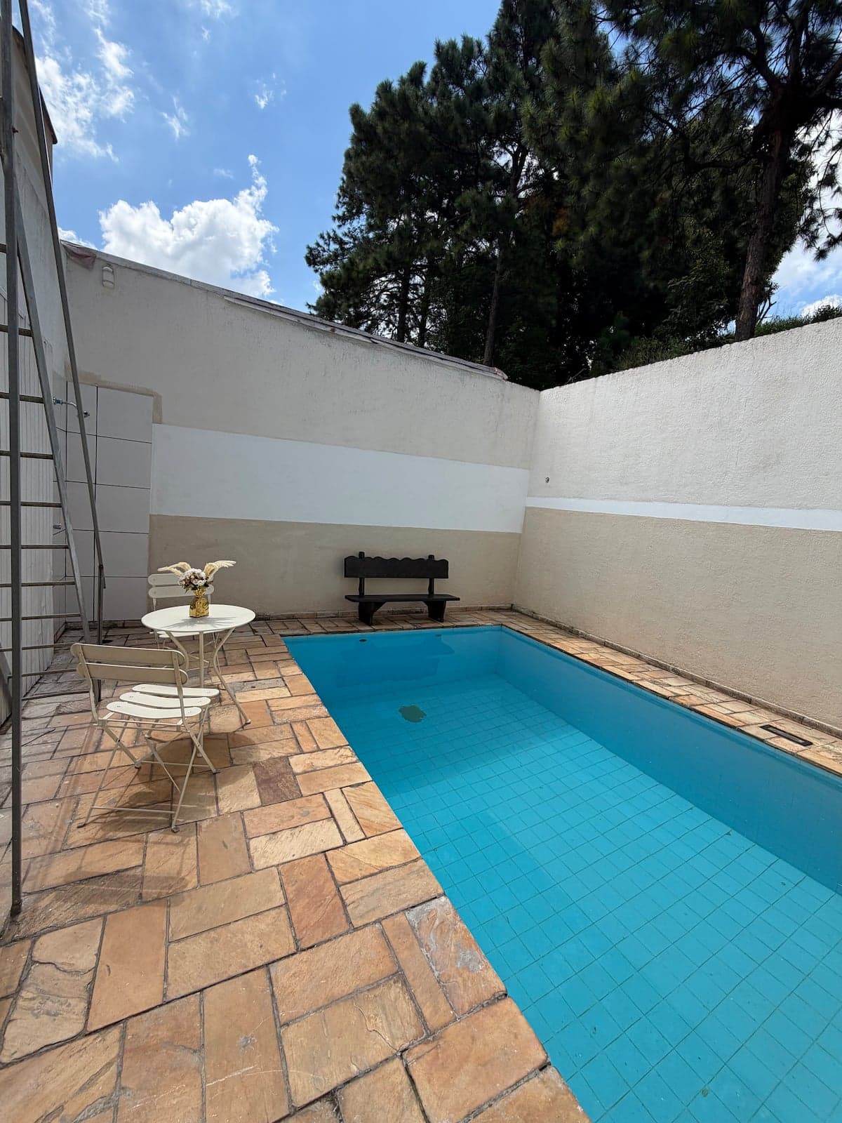 Piscina retangular com deck de pedra e mesa a sombra